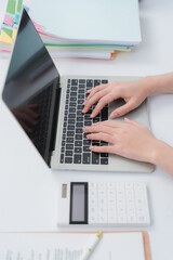 Fototapeta premium Hands typing on a laptop beside a calculator and documents, indicating productive work.