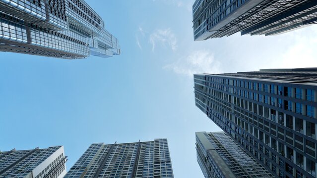 Low angle view of a modern glass skyscraper rising into a clear blue sky, featuring dramatic perspective, vertical lines, and generous copy space.