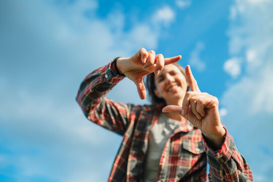 A smiling mature woman frames the blue summer sky with her hands