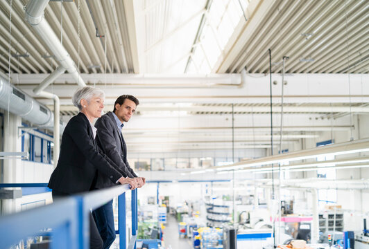 Senior businesswoman and businessman on upper floor in factory overlooking shop floor