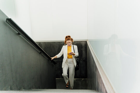 Businesswoman in white pant suit, ascending stairs, using smartphone