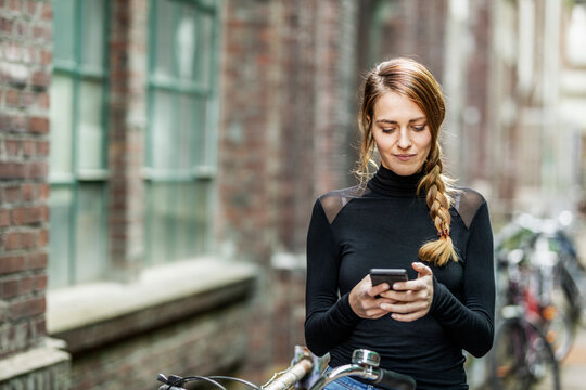 Portrait of woman with bicycle looking at cell phone
