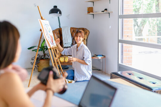 Smiling female painter looking at photographer colleague holding camera at studio