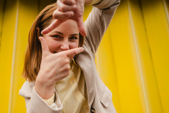 Smiling businesswoman making framing gesture against yellow background