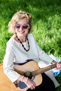 Smiling senior woman wearing sunglasses playing guitar in park
