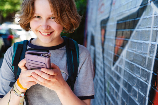 Smiling teenage girl holds a smartphone outdoors by a graffiti wall