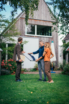 Real estate agent having discussion over solar panel with customers in back yard