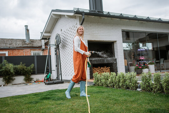 Smiling woman waters the green lawn with a hose in her backyard