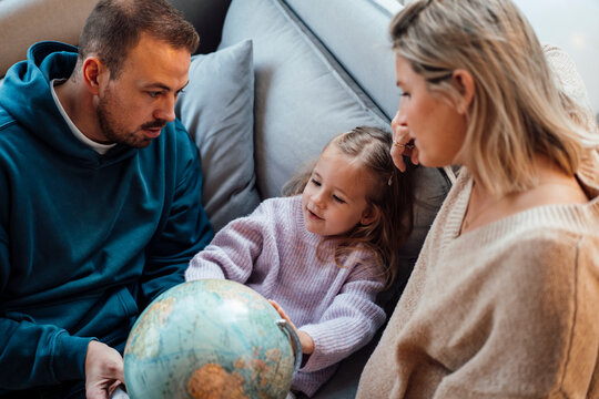 Daughter with parents looking at globe on sofa at home