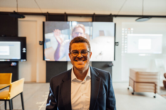 Smiling businessman stands in an office during a video conference