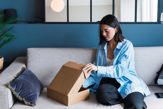 Young woman opening package on sofa at home