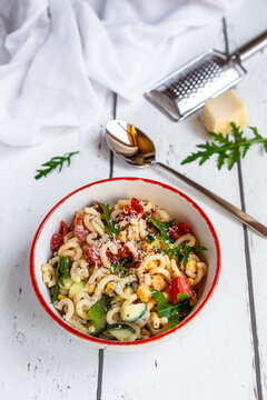 Bowl of noodle salad with corn, cucumber, tomatoes, rocket and grated parmesan