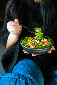 Woman eating mixed salad with lamb's lettuce, feta, pear, pomegranate seed and walnuts