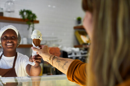 Young woman working in ice cream parlour, handing over icecream cone to customer