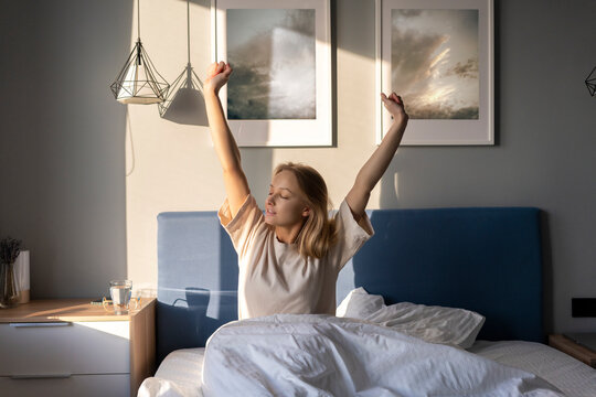 Young woman stretching arms while sitting on bed at home