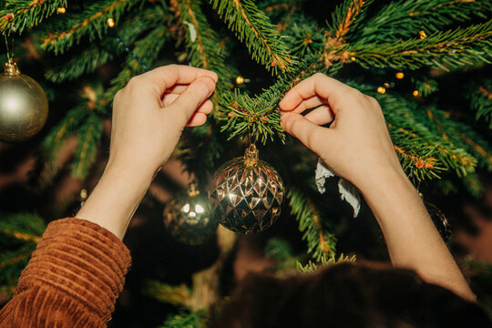 Boy hangs a gold bauble on the Christmas tree indoors