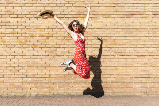 Happy young woman jumping and holding a straw hat