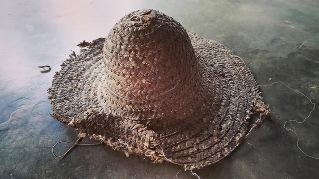 A weathered vintage straw hat lying flat on a textured concrete floor surface indoors