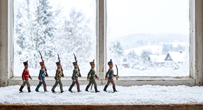 Row of vintage lead soldier figurines marching on a snowy windowsill against a frosty winter window. Miniature army toy display for Christmas decoration and vintage childhood nostalgia concept.