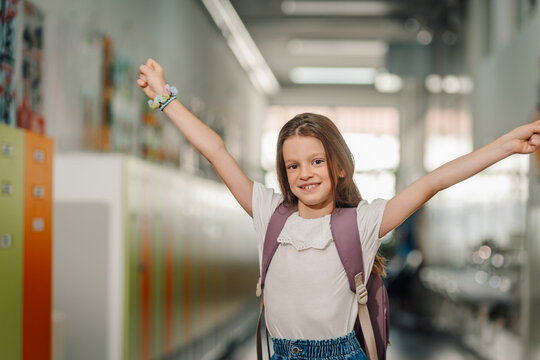 Happy schoolgirl raising arms celebrating success in hallway