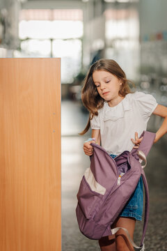 Young girl student holding backpack in school hallway