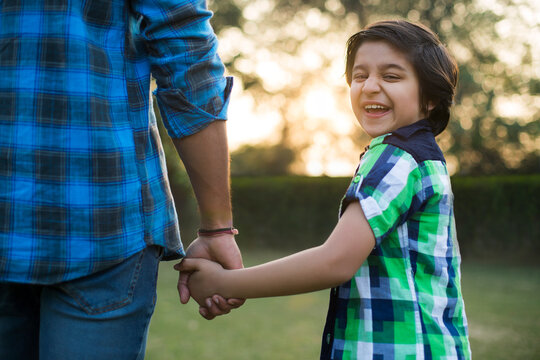 Rear view of a smiling boy holding hand of his father standing in park.