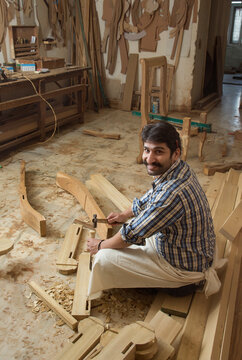 Smiling carpenter working on wood with a chisel and hammer sitting in his workshop.