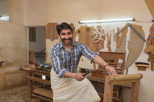 Happy carpenter hitting a nail with hammer in his workshop.