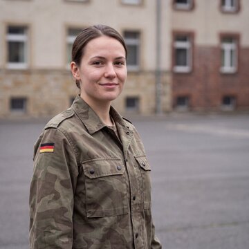 Junge Soldatin l&auml;chelt im Portr&auml;t auf dem Kasernenhof