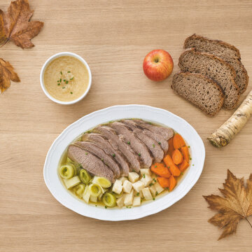 Plato de taфельшпиц con carne de res, verduras y salsa servido con pan y manzana