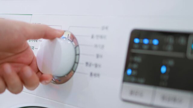 A close-up of the dial and control buttons on the front panel of a white washing machine with blue indicator lights.