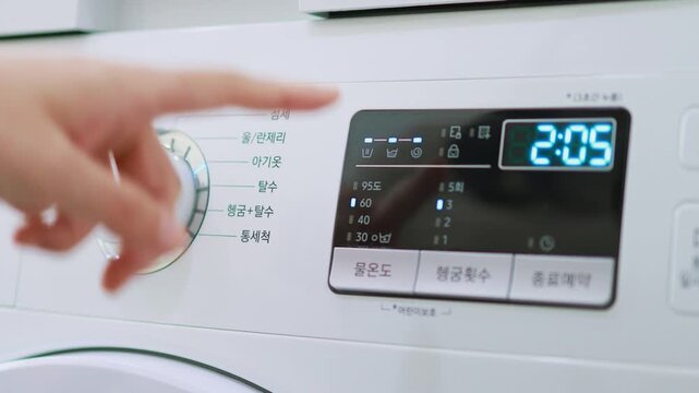 A close-up of the control panel of a white washing machine showing a digital time display and program selection dial.