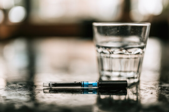 Insulin pen glass of water medical device table close up medication diabetes injection treatment healthcare still life clear glass bistro restaurant morning light natural light shallow depth