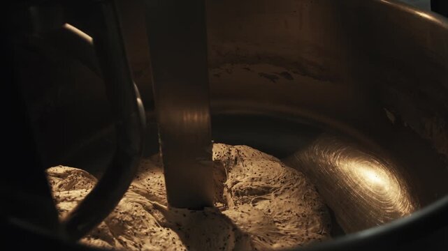 Ready dough with black seeds blended by industrial mixer in large stainless steel bowl. Process of bread making in private bakery, preparation of fresh baked goods. Culinary art of bread production