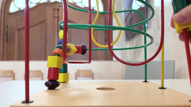 A close-up view of a hand moving colorful wooden beads along a classic bead maze toy in a hospital waiting room. Extreme close-up static shot filmed at eye level with the toy.