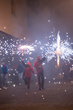 People in devil costumes performance with fireworks sparks on city street night view.
