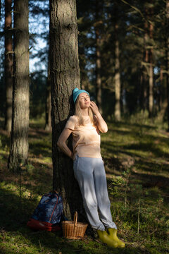 Relaxed thoughtful woman leaning on tree trunk in autumn forest, resting after foraging mushrooms in basket. Female recreating in woods outside city on weekend spend day, enjoying nature and silence