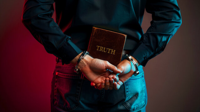 Man in handcuffs holding a book titled Truth behind his back. Restrained subject under dramatic cinematic lighting. Censorship and suppressed information concept for legal or human rights themes.