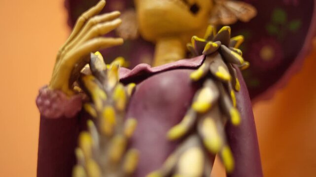 Closeup of handmade Catrina sculpture with moth decorations and floral hat, macro descend along dress and snake garment ornament