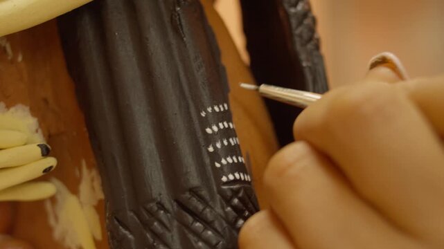 Close macro details of artisan painting white dot pattern on black garment details on clay Catrina sculpture