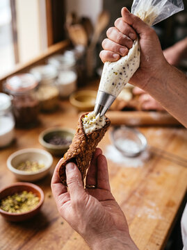 Pastry chef filling a traditional Sicilian cannoli shell with ricotta cream