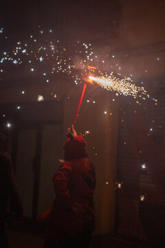 People in devil costumes performance with fireworks sparks on city street night view.

