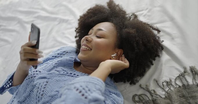 Portrait of young beautiful African black woman relax using ear bud listen to music from headphone in bedroom. Smile happy asian girl sing a song at home, Cheerful relaxing winter time