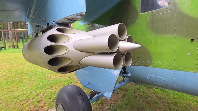 Military helicopter weapon pod close-up, rocket launcher system with multiple tubes visible, landing gear detail, static display outdoors on green grass, combat aircraft military vehicle.