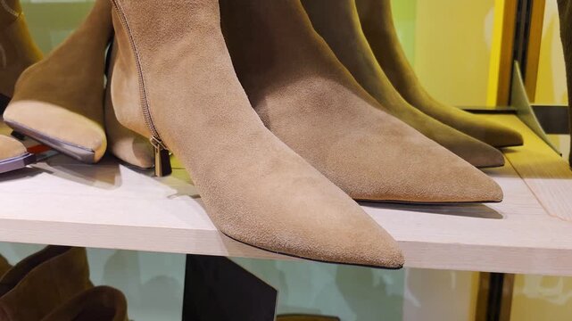 Collection of stylish brown suede ankle boots displayed on wooden shelf in retail store, featuring pointed toes and modern design, showcasing variety of fashionable footwear ready for purchase