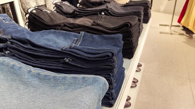 Multiple stacks of folded denim jeans in different shades of blue and black on display in a retail clothing store, presenting variety for purchase.