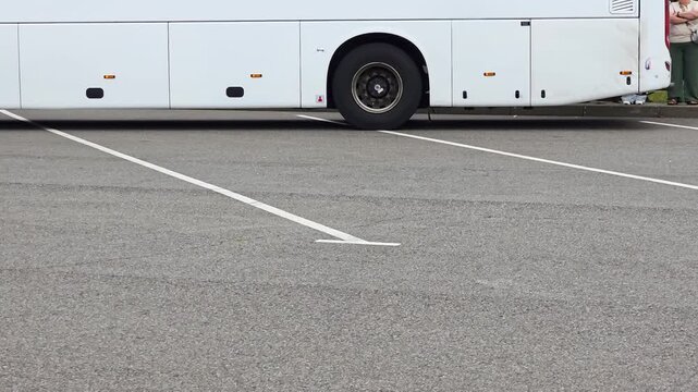 White coach bus side view parked in empty outdoor asphalt parking lot with white painted lines visible below vehicle. Focus on side of bus and ground, bus arrival at the station