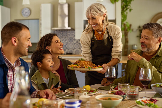 Happy latin senior woman serving food to her family at home