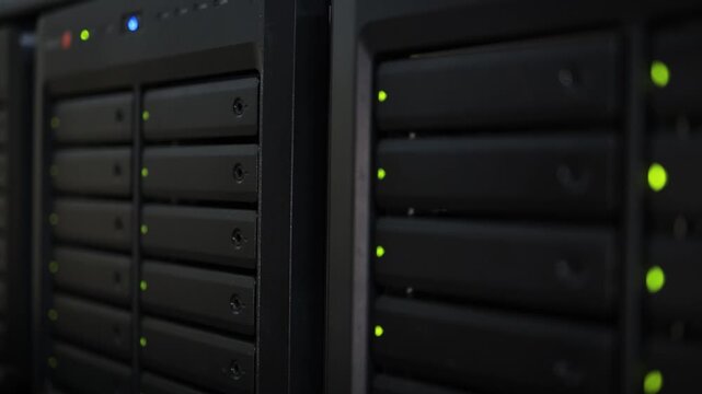 A wide view of stacked server rack units with green and yellow LED indicators glowing in a dark data center room.