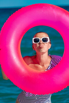 Playful woman looking through pink inflatable ring at the beach